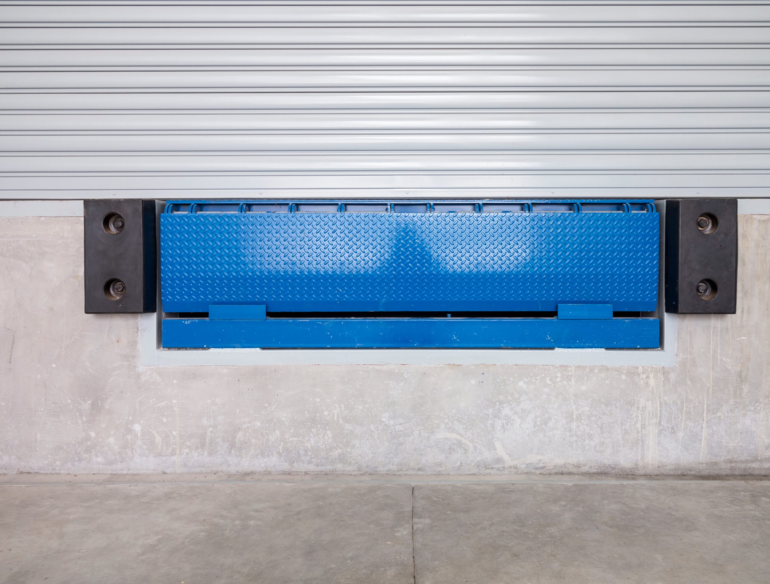 dock leveler or height adjustable platform outside warehouse or industrial building. used as bridge between dock and truck for loading, storage, warehousing, shipping and freight forwarding of cargo.